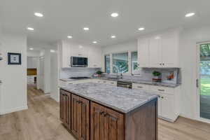 Kitchen with light stone counters, a center island, white cabinets, recessed lighting, and light wood-style flooring