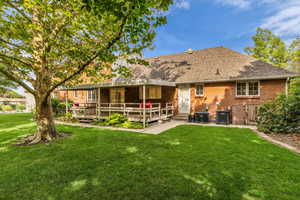 Rear view of house featuring brick siding, a lawn, roof with shingles, a deck, and a patio area