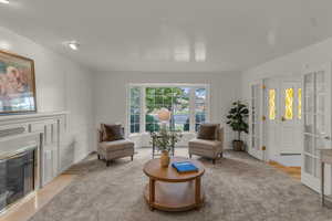 Living area featuring a fireplace with flush hearth, light carpet, a decorative wall, and french doors