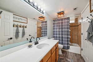 Full bath featuring a textured ceiling, dark wood-style floors, vanity, and shower / bath combination with curtain
