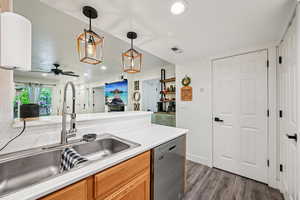 Kitchen featuring stainless steel dishwasher, light countertops, hanging light fixtures, dark wood-style flooring, and recessed lighting
