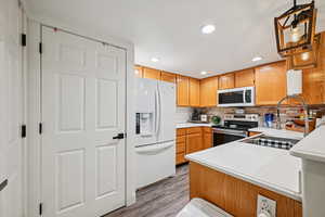 Kitchen with light countertops, white appliances, decorative backsplash, recessed lighting, and light wood-type flooring