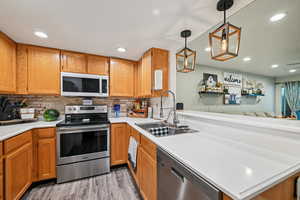 Kitchen with appliances with stainless steel finishes, hanging light fixtures, backsplash, light countertops, and light wood-style floors