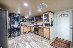 Kitchen featuring appliances with stainless steel finishes, light countertops, estacked washer and dryer, recessed lighting, and wall chimney range hood