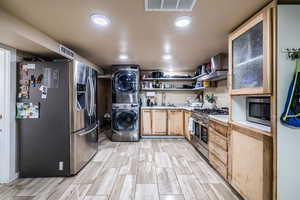 Kitchen featuring stainless steel appliances, light countertops, stacked washer / drying machine, recessed lighting, and light brown cabinets