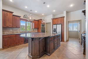 Kitchen with granite countertops, decorative light fixtures, decorative backsplash, an island with sink, and hardwood cabinets