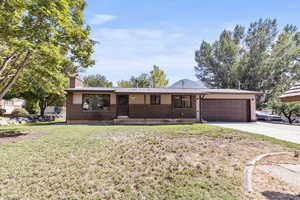 Single story home featuring a chimney, a front lawn, driveway, and brick siding