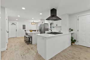 Kitchen with a kitchen breakfast bar, recessed lighting, a center island, island exhaust hood, and white cabinetry