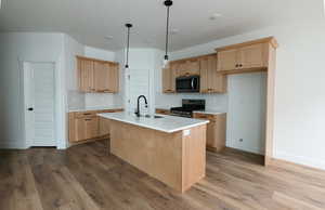 Kitchen featuring stainless steel range, hanging light fixtures, decorative backsplash, a center island with sink, and light brown cabinets