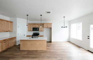 Kitchen with tasteful backsplash, light brown cabinets, light wood-type flooring, and a kitchen island with sink