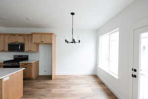 Kitchen featuring stainless steel range with gas cooktop, light wood-style flooring, pendant lighting, a chandelier, and tasteful backsplash