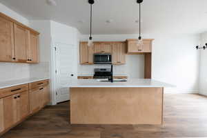 Kitchen featuring light brown cabinets, a center island with sink, backsplash, appliances with stainless steel finishes, and dark wood-style floors
