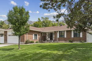 Ranch-style home with a front yard, brick siding, a mountain view, a garage, and concrete driveway