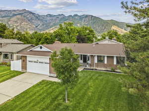 Ranch-style house featuring a mountain view, brick siding, a front lawn, concrete driveway, and a garage