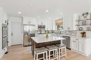 Kitchen with appliances with stainless steel finishes, a kitchen breakfast bar, white cabinetry, light wood-style floors, and a center island