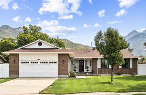 Ranch-style home with a mountain view, brick siding, roof with shingles, and concrete driveway