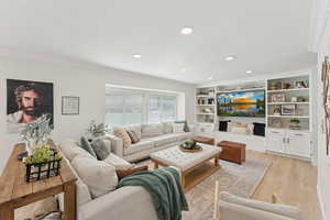 Living room featuring crown molding, light wood-type flooring, recessed lighting, and built in shelves