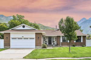 Ranch-style home featuring a mountain view, roof with shingles, driveway, brick siding, and an attached garage