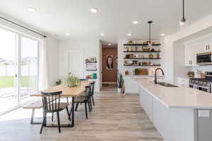 Kitchen with white cabinets, stainless steel appliances, recessed lighting, light wood finished floors, and decorative light fixtures