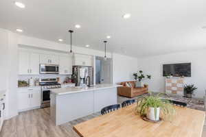 Kitchen with hanging light fixtures, stainless steel appliances, white cabinetry, decorative backsplash, and recessed lighting