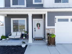Doorway to property with covered porch, stone siding, a garage, and board and batten siding