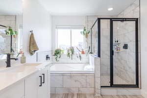 Bathroom featuring a stall shower, a garden tub, vanity, and wood finished floors
