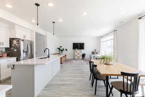 Kitchen featuring white cabinets, light wood finished floors, recessed lighting, decorative light fixtures, and stainless steel fridge