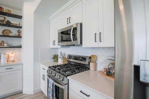 Kitchen featuring stainless steel appliances, backsplash, white cabinets, and open shelves