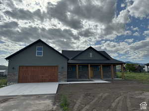 View of front of home with stone siding, driveway, covered porch, and a garage