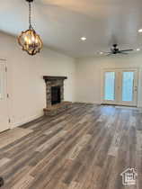 Unfurnished living room featuring a stone fireplace, recessed lighting, dark wood-type flooring, a ceiling fan, and a chandelier