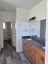 Full bathroom with double vanity, dark wood-style floors, and a spacious closet