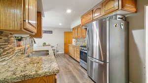 Kitchen featuring stainless steel appliances, tasteful backsplash, light stone counters, light wood-style flooring, and recessed lighting