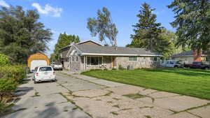 View of front of home with stone siding, an outbuilding, covered porch, concrete driveway, and a front lawn