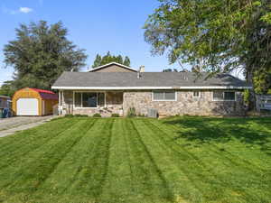 Ranch-style house featuring stone siding, an outdoor structure, and a front yard