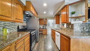 Kitchen featuring brown cabinets, light stone countertops, appliances with stainless steel finishes, tasteful backsplash, and light wood-style flooring