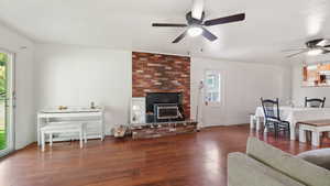 Living area with wood finished floors, plenty of natural light, a brick fireplace, and a ceiling fan