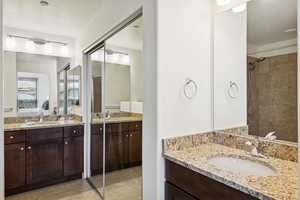 Bathroom featuring ensuite bathroom, a textured ceiling, two vanities, light tile patterned floors, and tiled shower