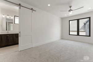 Unfurnished bedroom with light colored carpet, recessed lighting, ceiling fan, ensuite bathroom, and a barn door