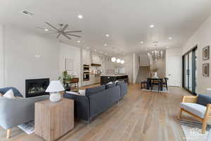 Living room featuring stairway, a tiled fireplace, light wood finished floors, recessed lighting, and a chandelier