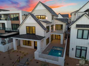 Back of house at dusk featuring a standing seam roof, board and batten siding, a metal roof, and a balcony