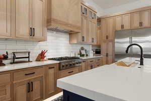 Kitchen featuring backsplash, appliances with stainless steel finishes, premium range hood, light stone countertops, and glass insert cabinets