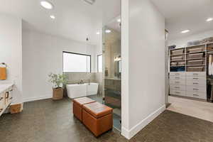 Bathroom featuring a shower stall, a freestanding tub, vanity, a walk in closet, and dark tile patterned flooring