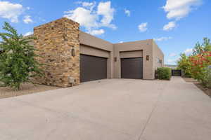 View of side of property with stucco siding, concrete driveway, an attached garage, and stone siding