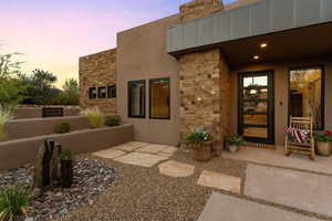 Doorway to property with stone siding, stucco siding, a chimney, and a patio