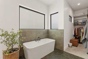 Full bathroom with a spacious closet, a freestanding tub, tile walls, and dark tile patterned floors