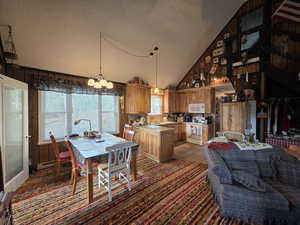 Dining area featuring a textured ceiling, high vaulted ceiling, a chandelier, wood walls, and a baseboard heating unit