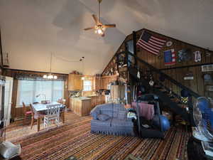 Carpeted living room featuring wood walls, high vaulted ceiling, a textured ceiling, ceiling fan, and a baseboard radiator