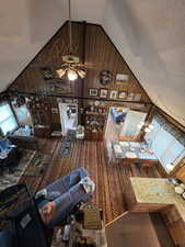 Living room featuring wooden walls, high vaulted ceiling, a textured ceiling, and a ceiling fan