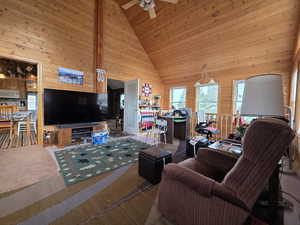 Carpeted living room featuring wood walls, high vaulted ceiling, wood ceiling, and a ceiling fan