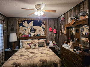 Bedroom featuring a textured ceiling, wood walls, and ceiling fan